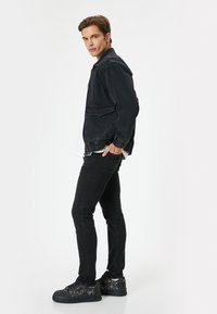 Chaqueta de mezclilla negra con puños elásticos, combinada con jeans ajustados negros y zapatillas oscuras con un diseño texturizado. Silueta simple y moderna.