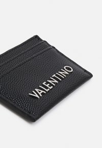Porte-cartes en cuir noir embossé avec quatre emplacements, affichant un logo « VALENTINO » en argent sur le devant. Texture lisse et design épuré.