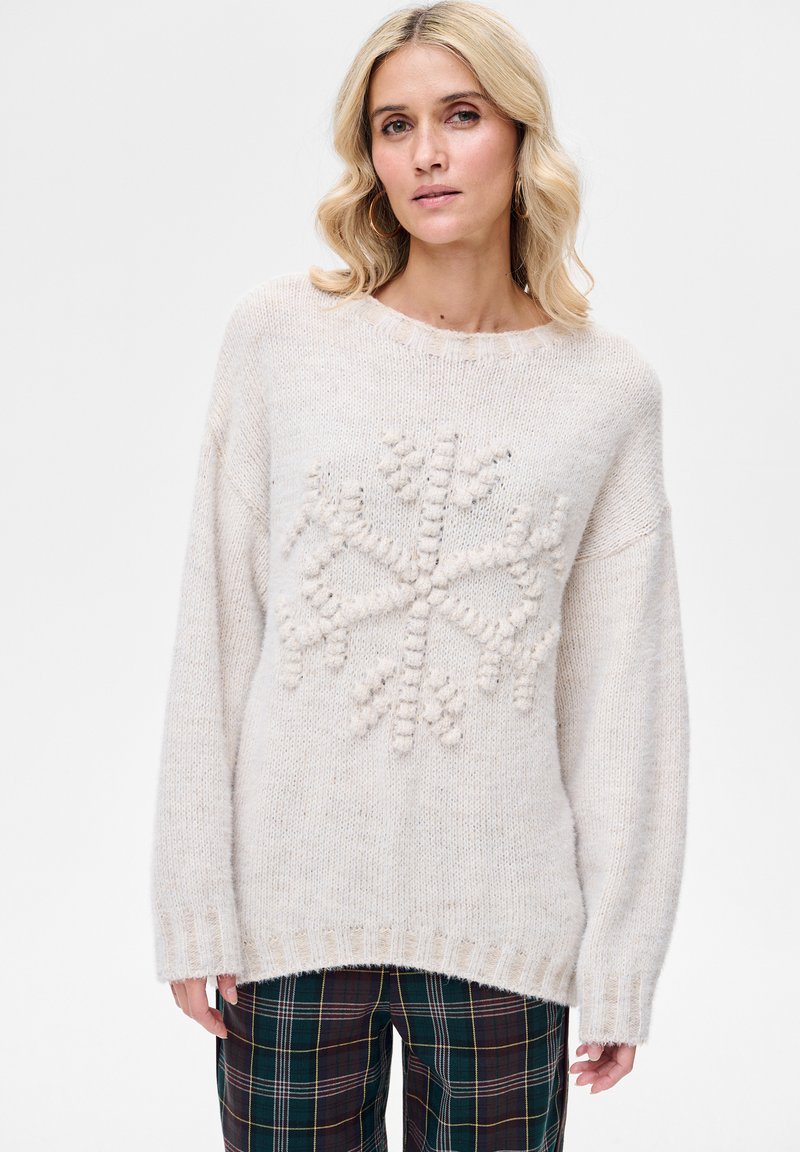 Jasnobeżowy sweter z teksturowanym wzorem płatka śniegu na środku. Charakteryzuje się luźnym krojem, ściągaczami na mankietach oraz szerokim dekoltem.