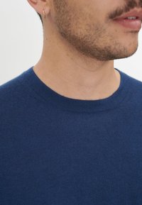 Marineblauer gestrickter Pullover mit rundem Ausschnitt und glatter Textur, Nahaufnahme des Kragens und des oberen Brustbereichs.