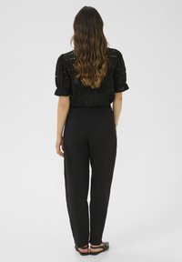 Blouse noire à manches courtes avec des détails en œillets, associée à un pantalon noir taille haute. Texture lisse, coupe décontractée et coutures minimales.