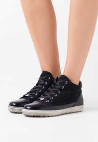 Marina högskor i mocka och lackläder, med runda snören, en texturerad sula och metalliska detaljer på tåskyddet.