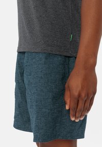 Chemise à manches courtes rayée grise avec un logo VAUDE, assortie de shorts texturés bleu sarcelle foncé. Les deux pièces présentent une coupe décontractée et relaxée.