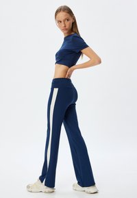Navyblauwe cropped top en bijpassende broek met een crèmekleurige zijstreep. Glad, rekbaar materiaal; aansluitend ontwerp met een zachte textuur.