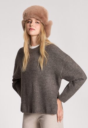 Maglione marrone a maglia con orlo e maniche a coste, abbinato a un cappello di pelliccia marrone chiaro con alette laterali. Lo sfondo è semplice.