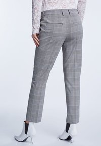Grijze geruite broek met een getailleerde pasvorm, met een middelhoge taille en achterzakken, gecombineerd met witte enkellaarsjes met hak.