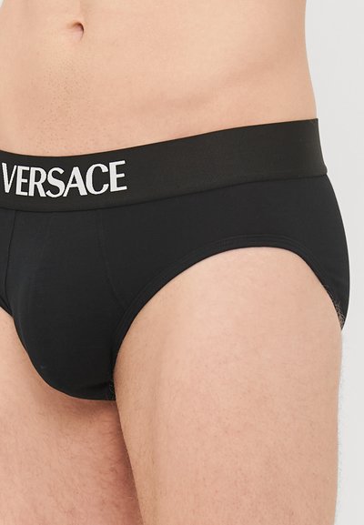 Boxer en coton noir avec une ceinture noire contrastante comportant l'inscription blanche "VERSACE". Texture lisse et design ajusté.