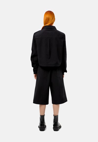 Zwarte cropped shirt en losse shorts van een duurzame stof, met een klassieke kraag en patchzakken, gecombineerd met zwarte enkellaarzen.