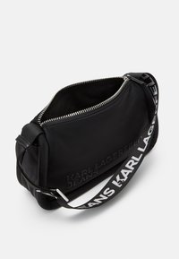 Fekete nylon táska cipzárral, dombornyomott logóval és kontrasztos szöveges pánttal. Puha tapintású, kompakt forma.