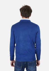 Maglione blu con maniche lunghe, polsini e orlo a coste, realizzato in morbido tessuto a maglia, indossato sopra una camicia con colletto, visto da dietro.