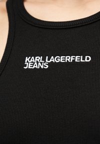 Μαύρο ριμπ αμάνικο τοπ με στρογγυλή λαιμόκοψη, διακοσμημένο με λευκή κεντημένη επιγραφή "KARL LAGERFELD JEANS" στο μπροστινό μέρος.