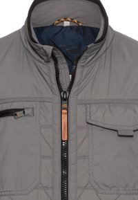 Graue gesteppte Jacke mit hohem Kragen, Frontreißverschluss und Brusttasche. Mit schwarzen Akzenten und einem Leder-Brand-Tag. Glatte Textur.
