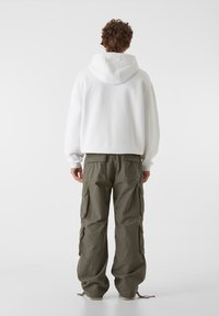 Biała bluza dresowa, wykonana z miękkiego materiału; zestawiona z oliwkowymi spodniami cargo, które mają wiele bocznych kieszeni i luźny krój.
