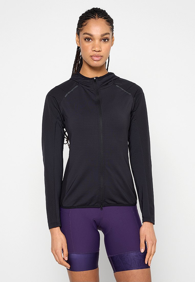 Veste noire zippée avec manches longues, tissu texturé et accents réfléchissants sur les épaules, associée à un short violet avec un ourlet à motif.