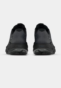 Must musta mustad jalanõud, nähtud tagant, tekstuursete tallade ja pehmendatud pahkluukatega, valgel taustal.