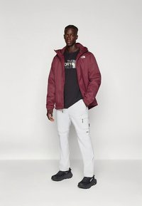 Tumedat värvi isoleeritud kapuutsiga jope, musta logoga t-särk, valged taskutega caro-püksid ja mustad spordijalatsid. Lihtne disain ja praktilised detailid.