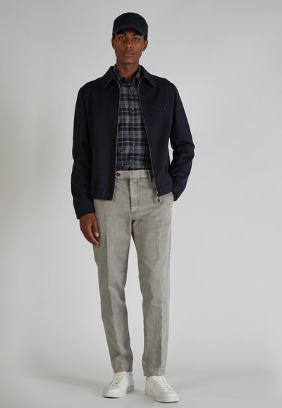Conjunto casual que incluye una chaqueta azul marino, una camisa de cuadros en azul y verde, pantalones gris claro y zapatillas blancas. Texturas claras y colores contrastantes.