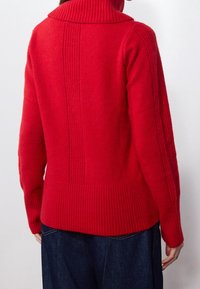 Czerwony sweter z prążkowanym kołnierzem, teksturowanym ciałem i pionowymi detalami prążkowania z tyłu. Ciepły materiał z mieszanki wełny.