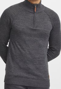 Dunkelgrauer Strickpullover mit hohem Kragen, Viertel-Reißverschluss und geripptem Saum. Verfügt über Raglanärmel und dezente texturale Variationen im Stoff.