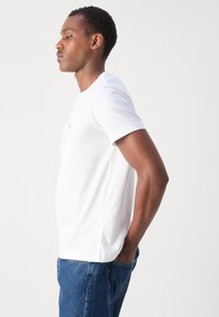 Hvid bomulds-T-shirt med rund hals, korte ærmer og en tætsiddende silhuet. Har et diskret logo på brystet og en glat tekstur.