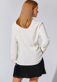 Hvid langærmet bluse med en glat tekstur, skræddersyet pasform og afrundet kant, parret med en sort satin miniskirt.