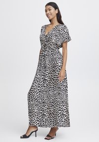 Leopardmönstrad maxiklänning med djup V-ringning, korta ärmar, elastisk midja, flytande tyg och en mjuk textur; bärs med svarta klacksandaler.