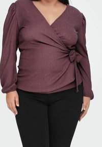 Bordeaux wikkeltop met gestructureerde stof, V-hals en lange mouwen met geplooide details en een zijstrikaccent. Gecombineerd met zwarte broek.