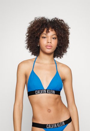 Blaues Triangle-Bralette mit dünnen Trägern und einem schwarzen Calvin Klein Logo-Band am unteren Rand. Glatter Stoff, minimalistisches Design.