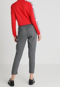 Röd långärmad topp med vit text på ärmarna, tillsammans med grå rutiga byxor och svarta skor. Enkelt mönster, elastisk midja på byxorna.