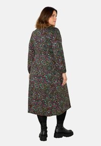 Černé šaty s vzorem, které se vyznačují živými květinovými a paisley vzory, dlouhými rukávy a volným siluetou; doplněné černými kotníkovými botami.