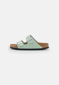 Green suede two-strap sandal with adjustable buckles, cork footbed, and black rubber sole. Flat design for comfort and support.