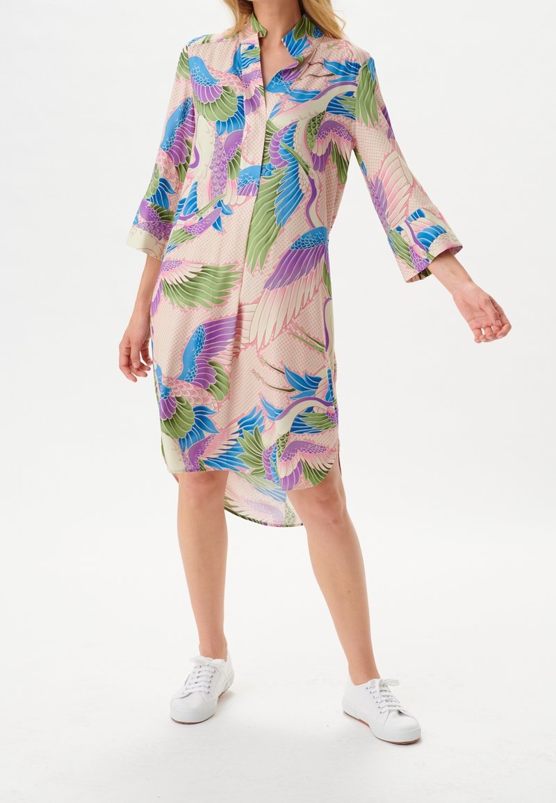 Vestito colorato con stampa di uccelli in turchese, verde e rosa su uno sfondo chiaro. Maniche lunghe e colletto. Tessuto morbido.