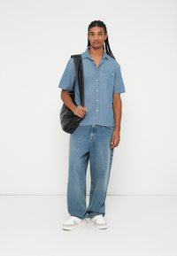 Cămașă din denim cu mânecă scurtă, de culoare albastru deschis, cu croială lejeră, prevăzută cu un buzunar frontal; asortată cu blugi albaștri cu croială largă și tenisi albi. Geantă neagră purtată peste umăr.