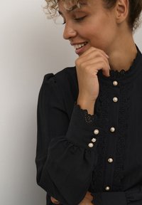 Black blouse with lace trim, pearl-like buttons, and puffed sleeves. Features intricate detailing and a high collar design.