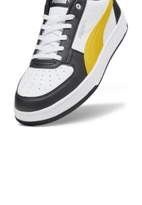 PUMA tenisky s černo-bílým svrškem a žlutým akcentem, s šněrováním, perforovanou špičkou a texturovanou gumovou podrážkou.