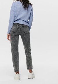 Verbleekte zwarte jeans met een rechte pijp, voorzien van twee achterzakken en contrasterende stiksels, gecombineerd met een lichtblauwe trui.