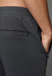 Donkergrijze sportshorts van een textuurstof, met een elastische tailleband en een zijzak. Het ontwerp is gericht op comfort en functionaliteit.