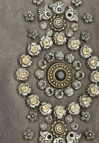 Elementi decorativi in metallo con tonalità d'oro e d'argento, numerosi accenti in cristallo, forme floreali e dettagli intricati su una superficie grigia testurizzata.