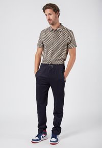 Koszula z krótkim rękawem w wielokolorowy geometryczny wzór, w połączeniu z granatowymi spodniami tapered i niebieskimi trampkami z czerwonymi akcentami.