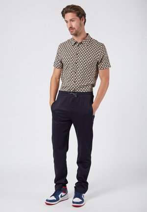 Camisa de manga corta con un patrón geométrico multicolor, combinada con pantalones tapered en azul marino y zapatillas azules con acentos rojos.