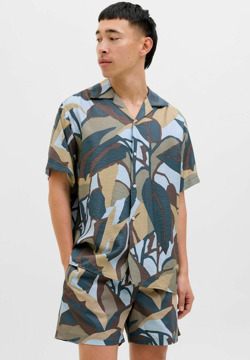 Sæt bestående af kortærmet skjorte og shorts i et bladrigt camouflage-mønster med nuancer af grøn, brun og blå, lavet af letvægtsstof.