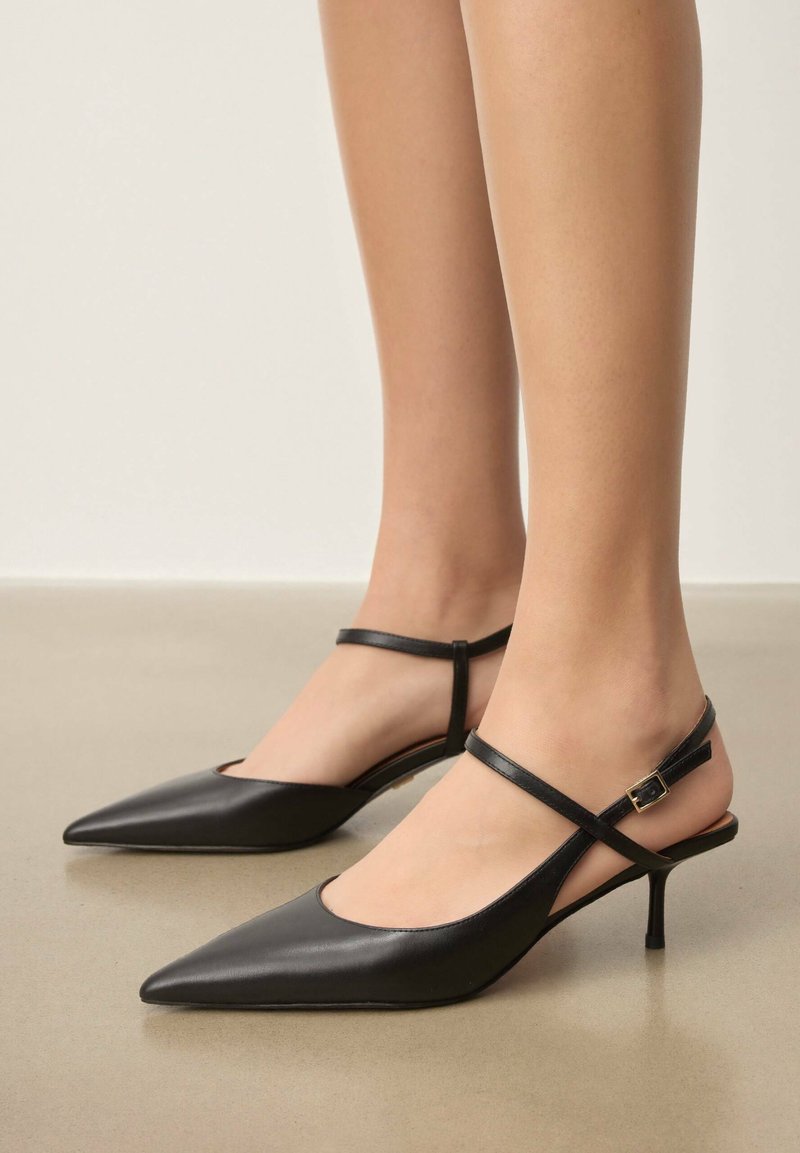 Chaussures slingback en cuir noir avec un bout pointu, dotées d'une fine bride à la cheville et d'un petit talon. Texture lisse et design minimaliste.