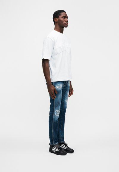 Λευκό κοντομάνικο μπλουζάκι με ανάγλυφο κείμενο, συνδυασμένο με σκισμένο μπουφάν τζην σε μπλε απόχρωση και μαύρα παπούτσια με λευκές ρίγες. Ύφασμα ομαλό και άνετη, casual εφαρμογή.