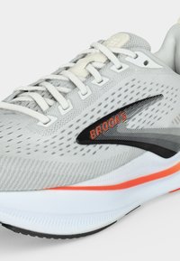 Light gray Brooks running shoe with white laces, black and orange logo, and white sole with orange accent stripe.