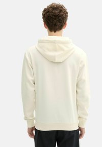 Sudadera con capucha cremosa, con puños y dobladillo acanalados. Tejido suave, diseño sencillo y cuenta con una gran capucha trasera. Sin logotipos ni patrones visibles.