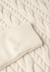 Cremfarbener Kabelstrickpullover mit weicher Textur und geripptem Bündchen. Das Kabelmuster ist auffällig und verleiht dem Design Tiefe.