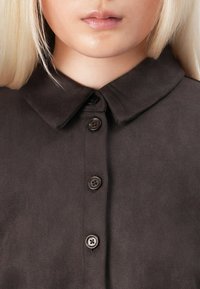 Brown suede shirt with a pointed collar, featuring four dark buttons down the front and a smooth texture.
