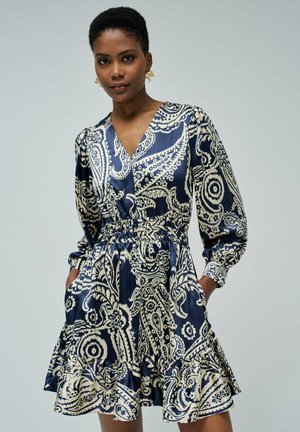 Vestido azul marino con patrón de paisley blanco, escote en V, mangas largas abullonadas, cintura elástica y dobladillo con volantes. Cuenta con bolsillos laterales.