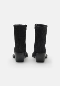 Botines de ante negro con una forma ligeramente acentuada, que cuentan con un cierre de cremallera y un tacón bloque brillante. Textura suave con un detalle mínimo.