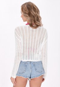 Cardigan alb, tricotat, cu un design cu țesătură deschisă, având mâneci lungi și o siluetă scurtă, asortat cu șorturi din denim.